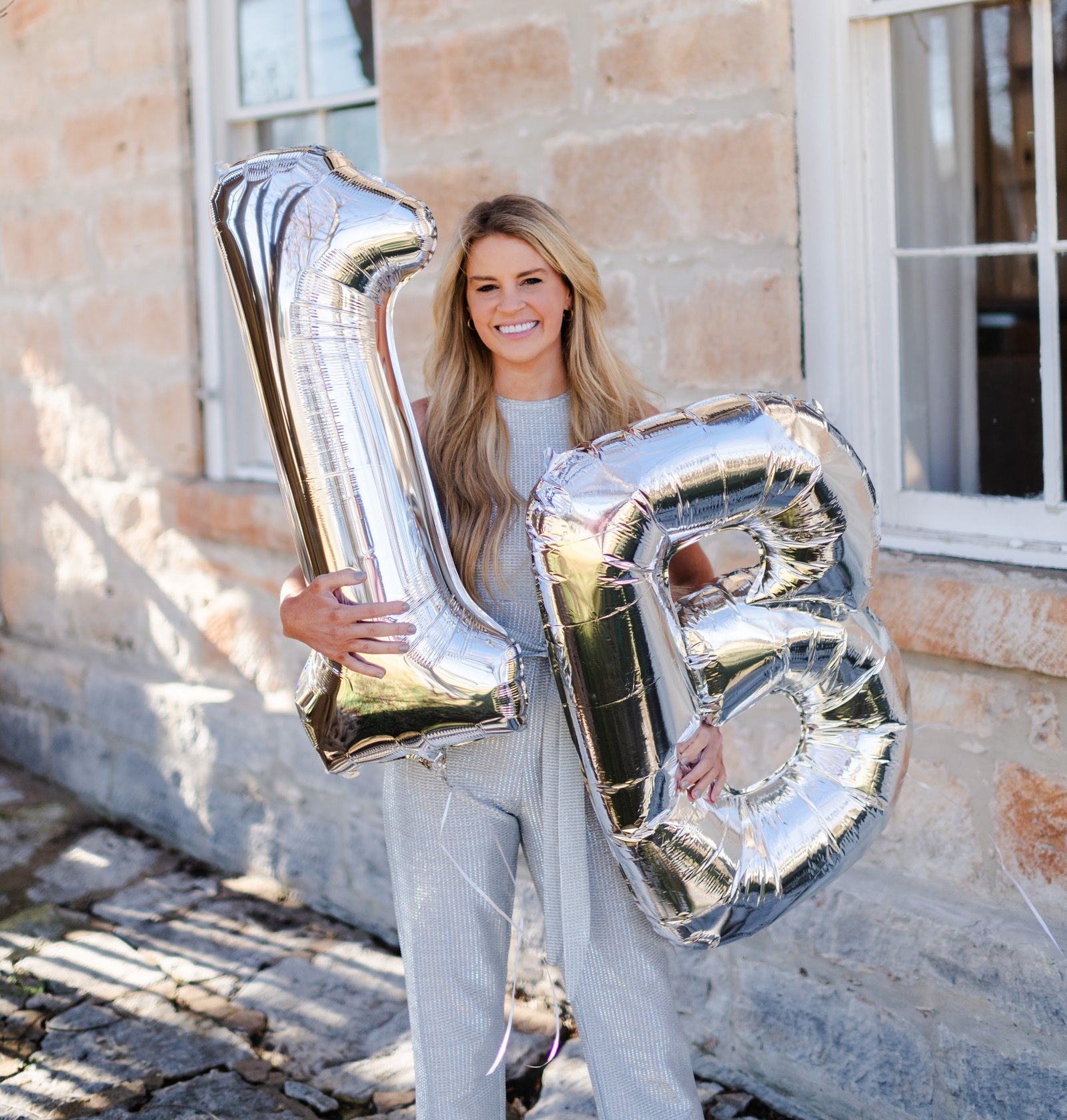 Savannah Sikes holding 1B balloons outside the limestone Absolute Charm Real Estate office in Fredericksburg