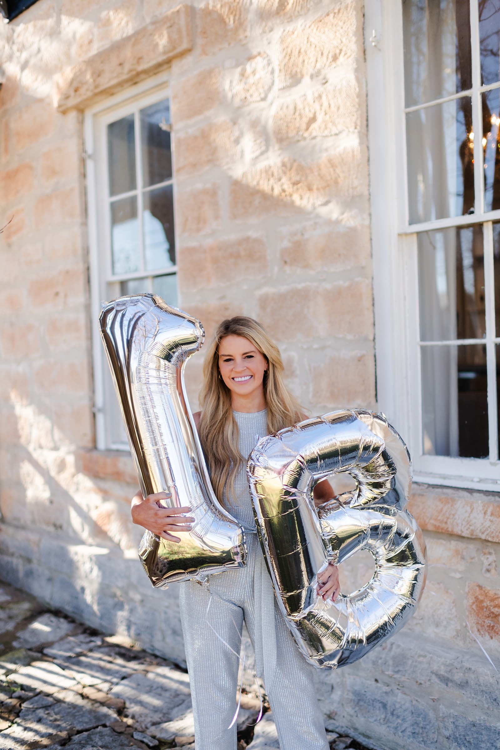 Savannah Sikes holding 1B balloons outside the limestone Absolute Charm Real Estate office in Fredericksburg