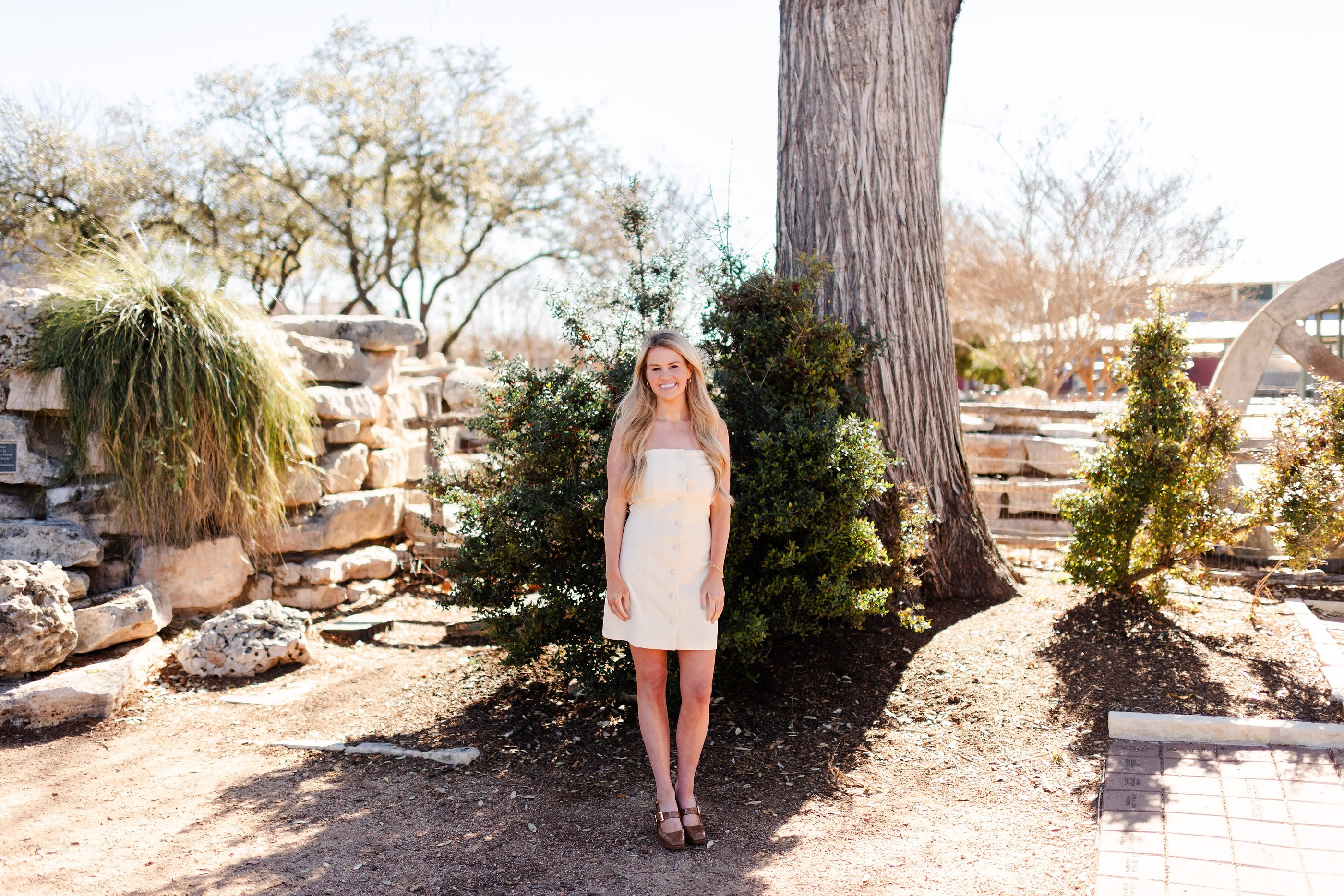 Savannah Sikes, Fredericksburg REALTOR®, in a cream dress beside a live oak in Fredericksburg, Texas